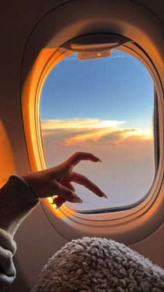 a person's hand reaching out the window of an airplane with clouds in the background