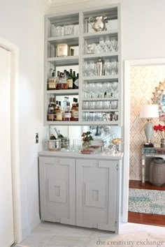 an open cabinet in the corner of a room filled with bottles and glasses on top of it