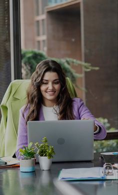 a woman sitting at a table with a laptop computer in front of her, smiling