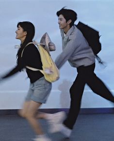 two people are running with an umbrella in their hand and one person is carrying a backpack