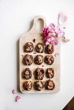 a wooden cutting board topped with lots of pastries next to a pink flower on top of a white table