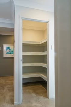 an empty walk in closet next to a doorway with shelves on both sides and one door open