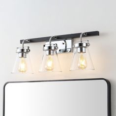 three light bathroom vanity fixture with clear glass shades and chrome finish, on a white wall