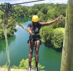 a woman is zipping through the air on a rope course with trees and water in the background