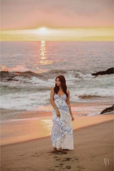 a woman standing on top of a sandy beach next to the ocean at sun set