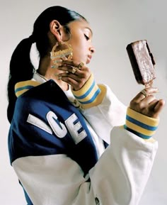 a woman holding a cell phone in her right hand and wearing a jacket with the word ice cream on it