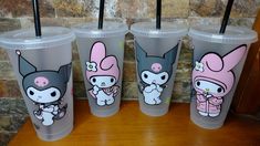 four plastic cups with cartoon characters on them sitting on a wooden table next to a brick wall