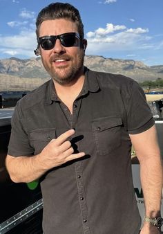 a man wearing sunglasses standing in front of a truck with his hand on the door