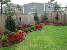 a garden with red flowers and green grass in the middle of it, next to a wooden fence