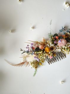 a hair comb with flowers and feathers on top of the comb is laying on a white surface