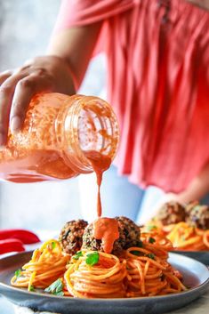 someone is pouring sauce over spaghetti on a plate with meatballs and carrots in the background