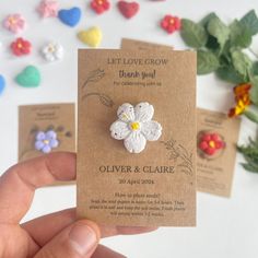 a person holding up two small flower brooches on top of a piece of paper