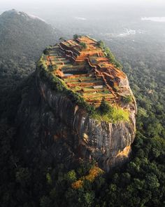 an aerial view of a rock formation in the middle of trees and mountains with grass growing on top