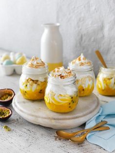 four mason jars filled with food sitting on top of a table next to spoons