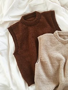 two sweaters sitting on top of a bed next to each other, one brown and one white