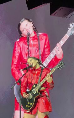 a man in red leather outfit holding a guitar and singing into a microphone on stage