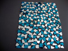 blue and white mosaic tiles are arranged on a black table top, with one square in the middle