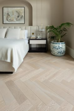 a large bed sitting in a bedroom next to a potted plant on top of a wooden floor