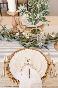 the table is set with white plates, silverware and greenery for an elegant look