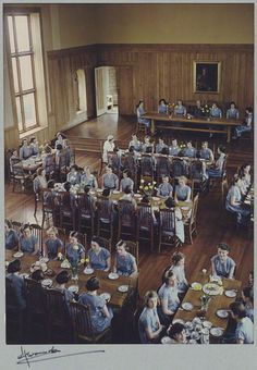 an old photo of people sitting at tables in a large room with wood paneling