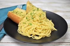 a black plate topped with spaghetti and bread