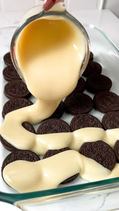 a glass dish with cookies and cream being poured into it, on top of some oreos