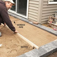 a man is laying sand on the ground and placing it in front of his house