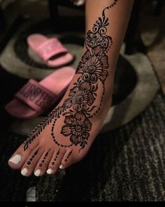 a woman's foot with henna tattoos on it and flowers around the toes