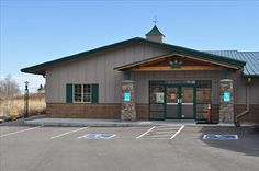 an empty parking lot in front of a building with a green roof and two doors