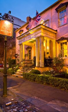 an old building lit up at night with street signs and bushes in front of it