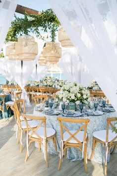 an outdoor dining area with blue and white table cloths, chairs, and chandeliers