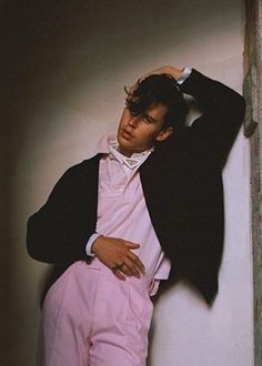 a man leaning against a wall with his hands on his head and wearing pink pants