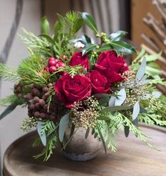 a vase filled with red roses on top of a wooden table covered in greenery