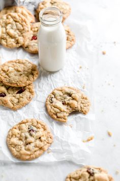 cookies with cranberries and oatmeal sitting on wax paper next to a bottle of milk