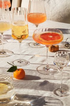 there are many glasses that have different drinks in them on top of a white table cloth