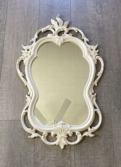 an ornate white framed mirror sitting on top of a wooden floor next to a wall