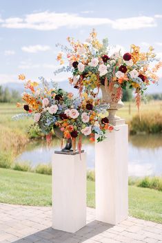 two vases with flowers are sitting on pedestals in front of a pond and grassy area