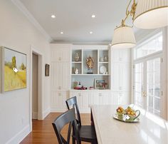 a kitchen with white cabinets and wooden flooring next to a dining room table filled with chairs