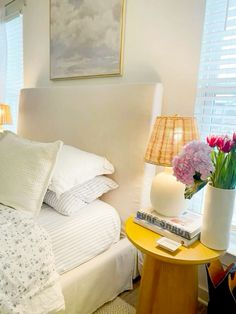 a bedroom with white bedding and flowers on the side table in front of it