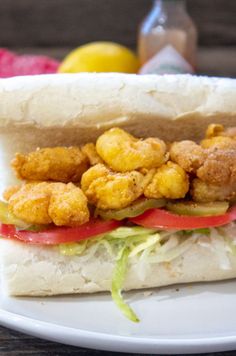 a sandwich with fried shrimp and lettuce sits on a plate next to lemons