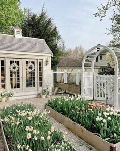 a garden with lots of flowers in it and a white building behind it that is surrounded by trees