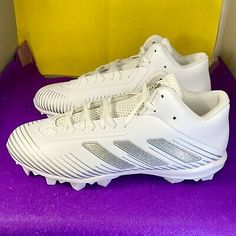 a pair of white adidas shoes sitting on top of a purple table next to a yellow box