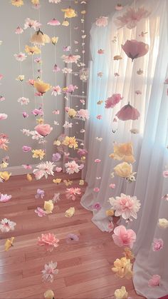 a room filled with lots of pink and yellow paper flowers hanging from the ceiling next to curtains