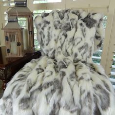 a bed covered in white and grey fur next to a window