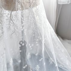 a cat sitting under a sheer curtain in front of a window with snowflakes on it