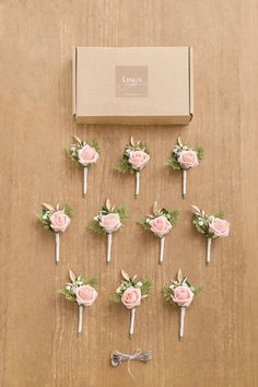 wedding boutonnieres with pink roses and greenery are arranged on a wooden table