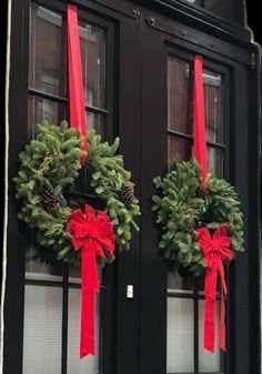 two wreaths on the front door of a house with red bows and pine cones