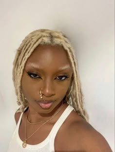 a woman with blonde dreadlocks wearing a white tank top and gold nose ring