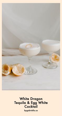 two glasses filled with white dragon tequila and egg white cocktails next to sliced lemons