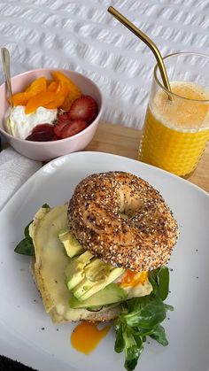 a bagel sandwich with avocado, cheese and strawberries next to a glass of orange juice